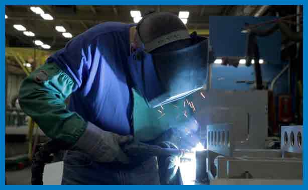 A man welding in an industrial setting with lights.